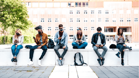 A group of students sitting outside of the university where all of them are using their phones.